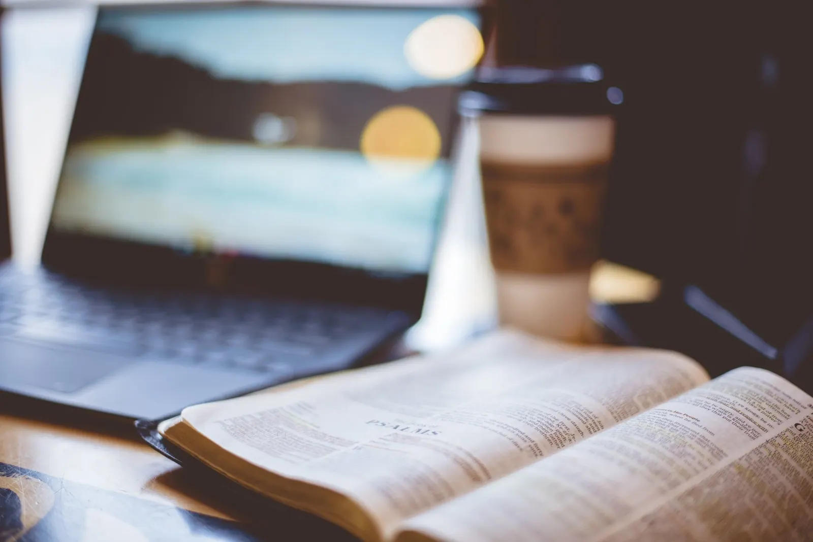 An open Bible beside a cup of coffee and a laptop