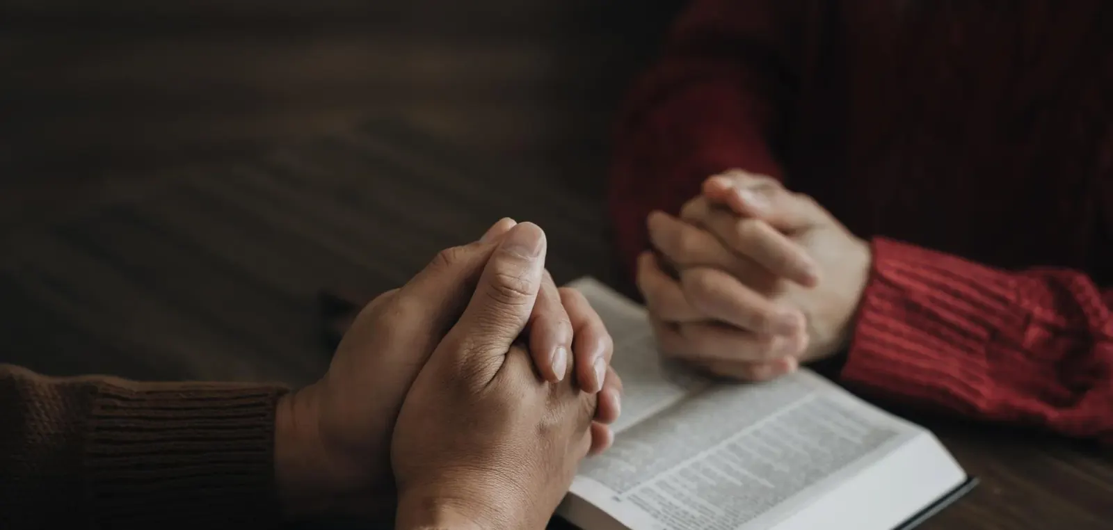 Hands folded in prayer on an open Bible